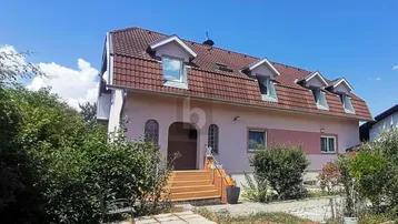 Einfamilienhaus mit Mansarddach und mehreren Gaubenfenstern unter blauem Himmel.