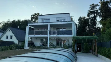 Modernes Mehrfamilienhaus mit mehreren Balkonen, einer Dachterrasse und einem überdachten Pool im Gartenbereich.
