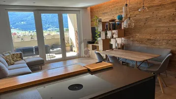 Moderner offener Wohnbereich mit Holzwand, integrierter Küche und Zugang zu einem Balkon mit Bergblick.