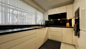 Moderne Küche mit weißen Hochglanzfronten, schwarzen Arbeitsplatten und Fliesenboden.