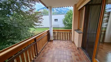 Geräumiger Balkon mit Holzgeländer, Fliesenboden und weitem Blick auf die Berge.