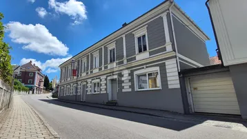 Historisches Gebäude mit grauer Fassade und weißen Verzierungen an einer ruhigen Straße.