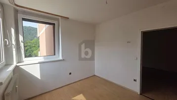 Unmöblierter Raum mit Laminatboden und Fensterblick ins Grüne, ideal für Schlaf- oder Arbeitszimmer.