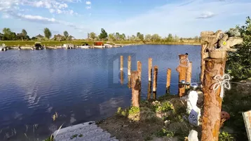 Weitläufiger Blick auf einen See mit Bootsanlegestellen und grüner Uferlandschaft unter blauem Himmel.