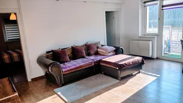 Helles Wohnzimmer mit bequemer Sitzecke, Laminatboden und Zugang zu einem sonnigen Außenbereich.