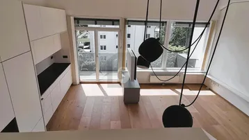 Heller Wohnbereich mit moderner Einbauküche, Holzboden und großen Fenstern zum Balkon.
