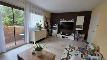 Helles Wohnzimmer mit Holzboden, brauner Akzentwand und Zugang zu einem möblierten Balkon.