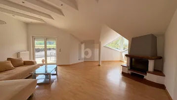 Geräumiges Wohnzimmer mit Holzboden, Kamin und Zugang zu einem sonnigen Balkon im Dachgeschoss.