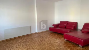 Geräumiges Wohnzimmer mit rotem Sofa und klassischem Parkettboden, bereit zur individuellen Gestaltung.