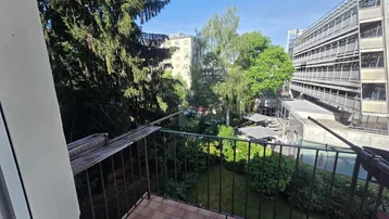 Kleiner Balkon mit Fliesenboden und Blick auf einen grünen Innenhof mit Bäumen.
