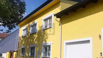 Gelbe Hausfassade mit weißen Fenstern und Garagentor unter blauem Himmel.