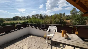 Großer Balkon mit Fliesenboden, Gartenmöbeln und weitem Blick ins Grüne und die Landschaft.