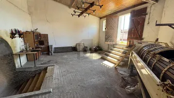 Großer, rustikaler Innenraum mit Holzbalkendecke, Steinstufen und einem alten Weinfass.