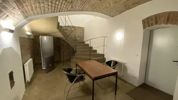 Gewölbekeller mit Backsteindecke, Steintreppe und einem Esstisch.