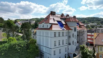 Historisches Gebäude mit Mansarddach und umliegender grüner Landschaft aus der Vogelperspektive.