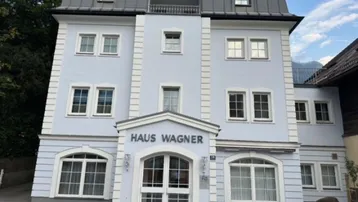 Das Gebäude 'Haus Wagner' präsentiert sich mit einer hellblauen Fassade und einem Mansarddach.