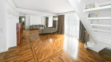 Helles Wohnzimmer mit elegantem Parkettboden, hohen Decken und einer stilvollen Treppe.