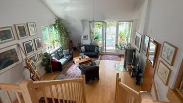 Geräumiger Wohnbereich mit hohen Decken, Holztreppe und Zugang zu einem Balkon.