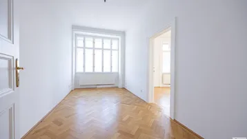 Helles Zimmer mit Fischgrätparkett und großen Fenstern, bereit zur individuellen Gestaltung.