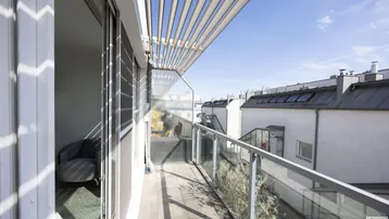 Helles Balkon mit Glasgeländer und Lamellendach, bietet einen Blick auf die umliegenden Gebäude.