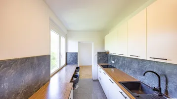 Moderne Küche mit weißen Schränken, Holzarbeitsplatten und einem langen Tresen mit Sitzgelegenheiten am Fenster.
