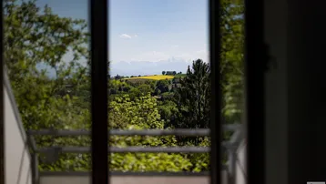 Panoramablick aus dem Fenster auf eine weite Landschaft mit grünen Hügeln und fernen Bergen.