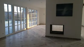 Heller Wohnbereich mit Kamin, großen Fenstern und Zugang zum Außenbereich.