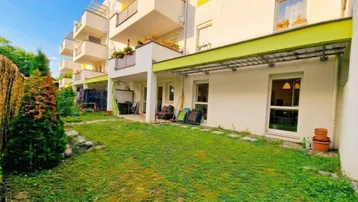 Gepflegter Gartenbereich mit Rasenfläche und überdachter Terrasse im Erdgeschoss eines modernen Mehrfamilienhauses.