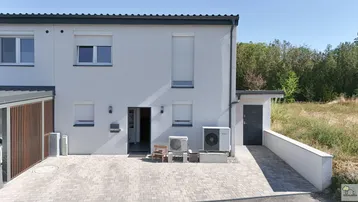 Vorderansicht eines modernen Reihenhauses mit gepflastertem Eingangsbereich und Wärmepumpe.