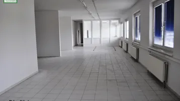Geräumige, leere Bürofläche mit hellen Fliesen und großen Fenstern, die viel Tageslicht hereinlassen.
