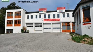 Gebäude G mit mehreren Garagentoren und Fenstern, umgeben von einem Vorbereich und einer Zufahrt.