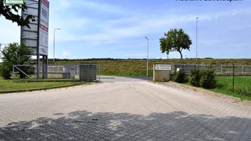 Ausfahrt eines Gewerbeparks mit gepflastertem Weg, Zaun und einem Schild mit Abschiedsgruß.