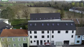 Luftaufnahme eines modernen Wohngebäudes mit umliegender Landschaft und weiteren Häusern.