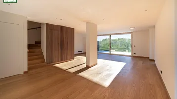 Helles, leeres Wohnzimmer mit Holzboden, großen Fenstern und moderner Holzwandverkleidung.