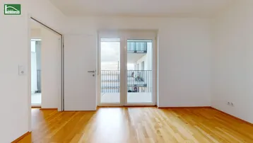 Helles, leeres Zimmer mit Parkettboden und Zugang zu einem Balkon, ideal für Wohn- oder Schlafbereich.