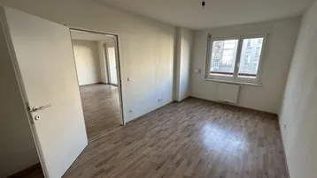 Heller, unmöblierter Raum mit Laminatboden und weiß gestrichenen Wänden, bereit zum Einzug.