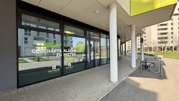 Moderne Geschäftsfassade mit großen Schaufenstern und Werbeaufklebern für Mietflächen im Erdgeschoss.