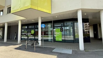Moderne Außenansicht eines Geschäftsgebäudes mit großen Glasfronten und einem gelben Balkon.
