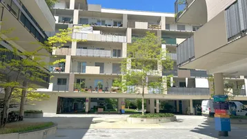 Moderner Apartmentkomplex mit mehreren Balkonen und einem begrünten Innenhof unter blauem Himmel.