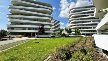 Moderne Wohngebäude mit geschwungenen Balkonen und gepflegten Grünflächen unter blauem Himmel.