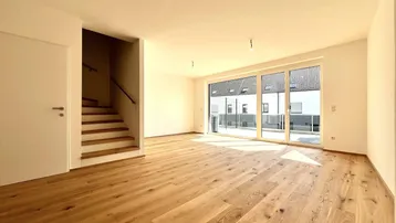 Helles Wohnzimmer mit Echtholzparkett, großen Fenstern und Zugang zu einem Außenbereich.