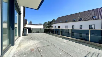 Große, unmöblierte Dachterrasse mit Blick auf umliegende Gebäude unter blauem Himmel.