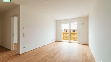 Helles, unmöbliertes Wohnzimmer mit Holzboden und Zugang zu einem Balkon.
