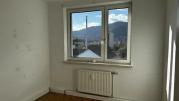 Helles Zimmer mit Parkettboden und Fensterblick auf die umliegende Berglandschaft.