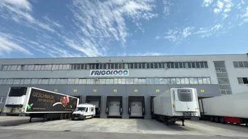 Großes Logistikzentrum mit mehreren Laderampen und Lastwagen unter blauem Himmel.