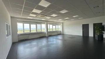 Großer, heller Büroraum mit dunklem Boden, Rasterdecke und weitem Ausblick durch die Fenster.