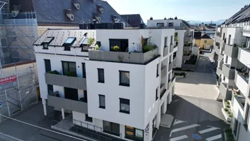 Luftaufnahme eines modernen Wohngebäudes mit Flachdach und Balkonen in städtischer Umgebung.