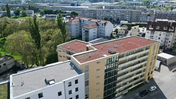 Vogelperspektive des Wohngebäudes mit begrüntem Flachdach und Blick auf die Stadt und Berge.