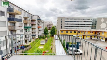 Blick vom Balkon auf den begrünten Innenhof mit Spielplatz und umliegende Gebäude.
