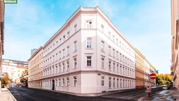Klassisches Eckgebäude mit heller Fassade und vielen Fenstern in urbaner Umgebung.